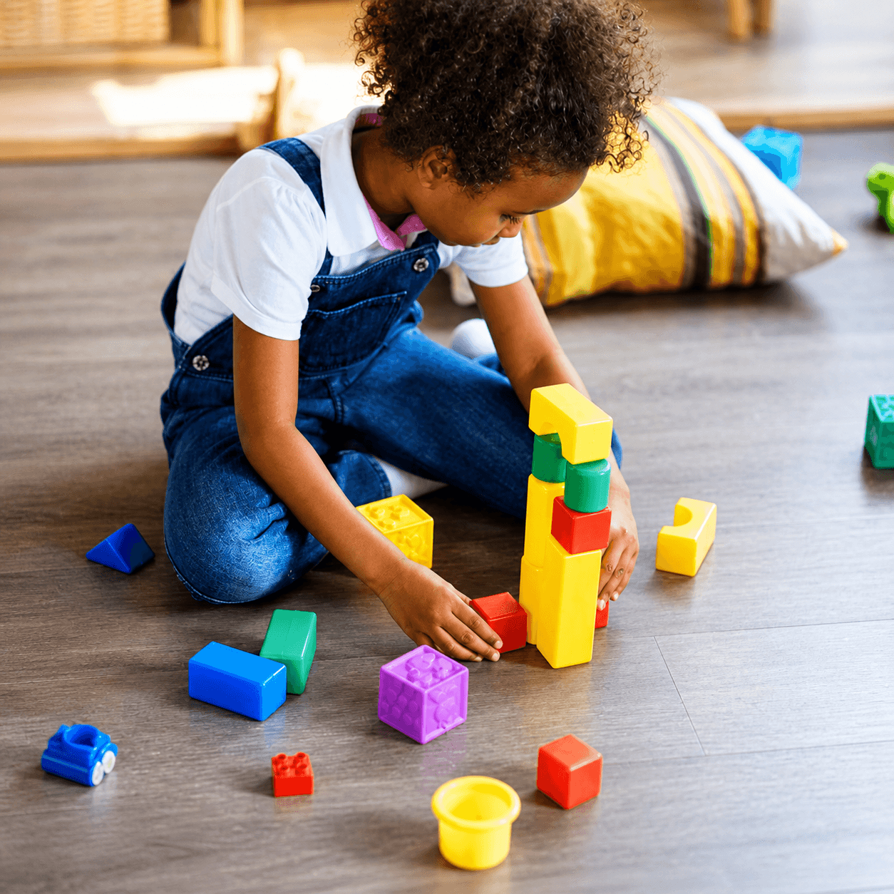 Young girl in overalls building a tower of plastic blocks during play-based therapy