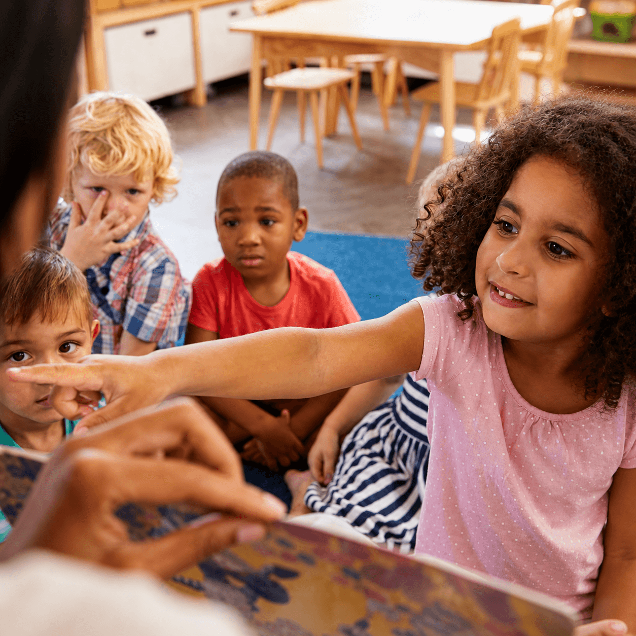 Preschoolers gathered on a classroom rug as a teacher points to a picture book during early intervention