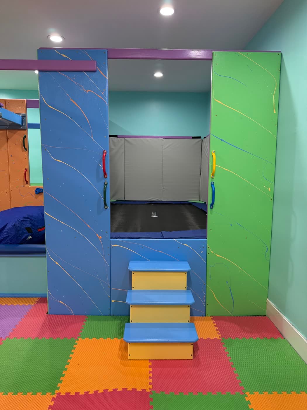 An enclosed alcove in the sensory gym with an indoor trampoline and padded steps